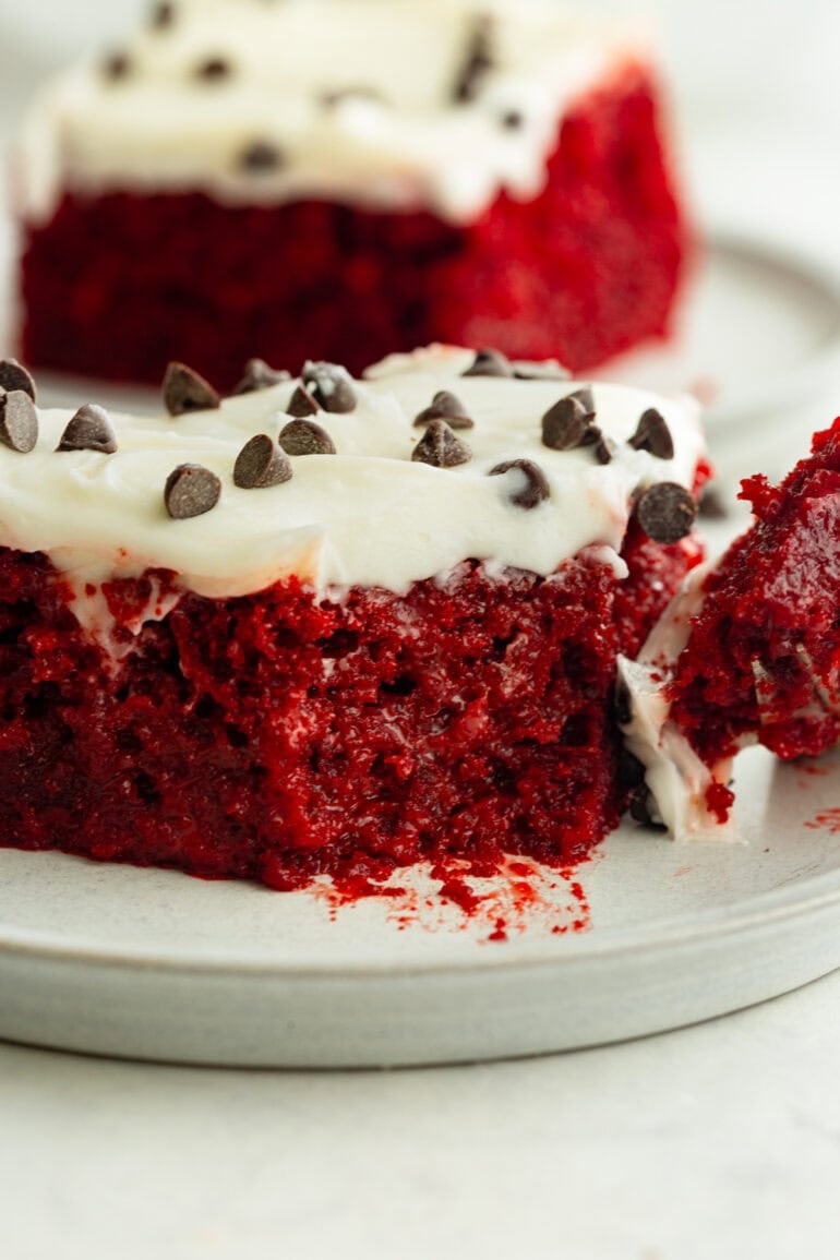 a piece of moist red velvet poke cake with a bite removed from the corner