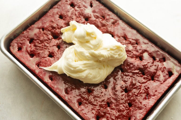 cream cheese frosting being spread on a red velvet poke cake