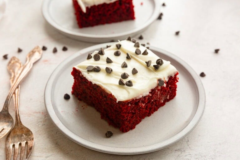a piece of red velvet cake with cream cheese frosting topped with mini chocolate chips on a small dessert plate
