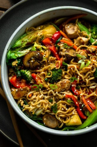a photo of a large bowl fill of yakisoba noodle with stir fried vegetables including red peppers, mushrooms, chicken chunks, baby bok choy