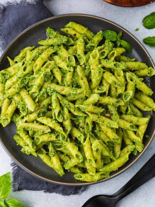 a close up photo of a plate full of bright green pesto covered penne pasta.