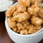 Crispy Honey Chicken in a white bowl next to a small bowl of white rice on a wooden table.