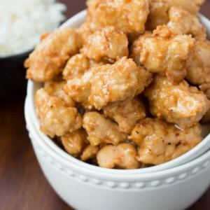 Crispy Honey Chicken in a white bowl next to a small bowl of white rice on a wooden table.