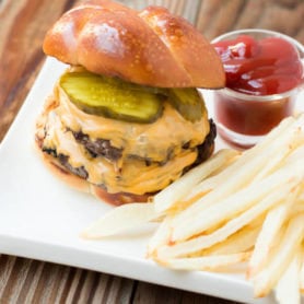 a cheeseburger with two patties, and pickles sitting next to french fries and a small cup of ketchup
