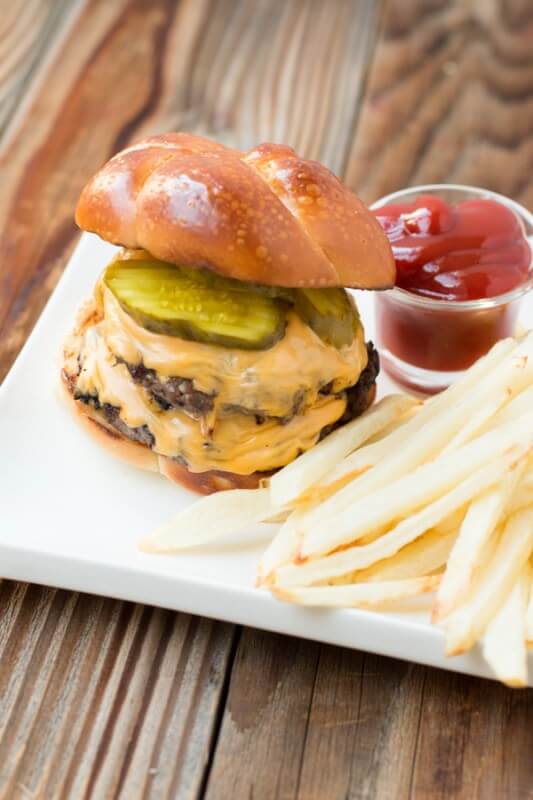 a cheeseburger with two patties, and pickles sitting next to french fries and a small cup of ketchup