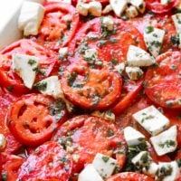 A photo of a marinated tomatoes salad with fresh herbs and 3 cheeses.