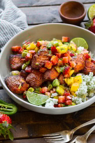 a photo of a bowl of seasoned salmon bites on top of rice and topped with strawberry mango avocado salsa