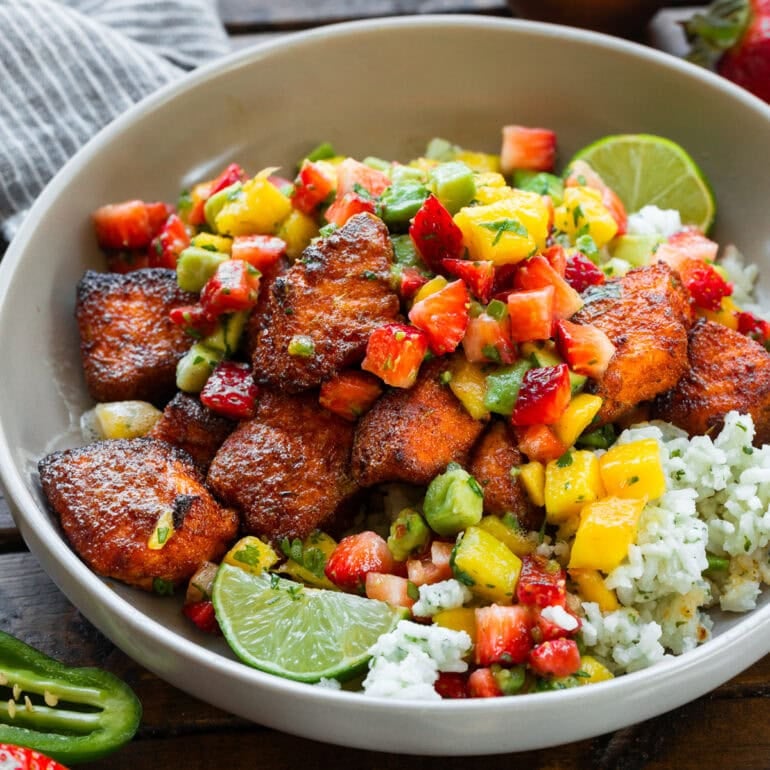 a photo of a bowl of seasoned salmon bites on top of rice and topped with strawberry mango avocado salsa