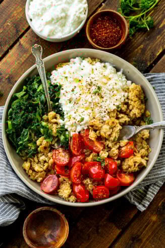 a photo of a bowl of crispy oats mixed with cherry tomatoes, cottage cheese, chopped kale and minced herbs