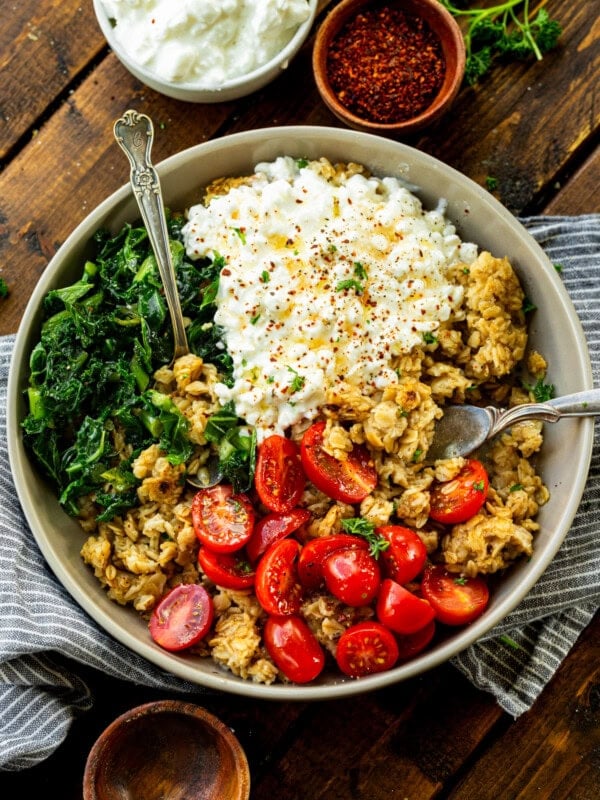 a photo of a bowl of crispy oats mixed with cherry tomatoes, cottage cheese, chopped kale and minced herbs