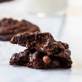 A chocolate, chocolate chip cookie broken in half showing the gooey chocolate chips inside