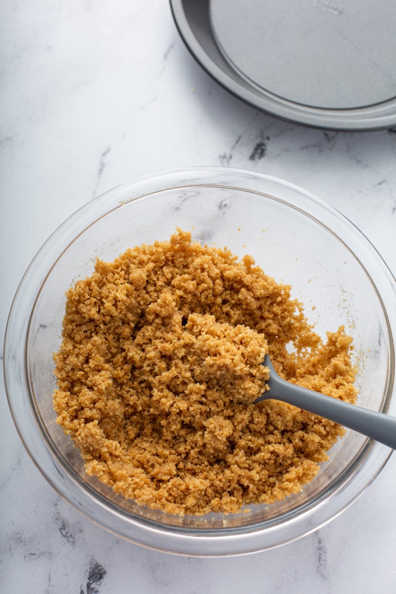 Crushed graham cracker crumbs and melted butter being stirred together in a bowl.