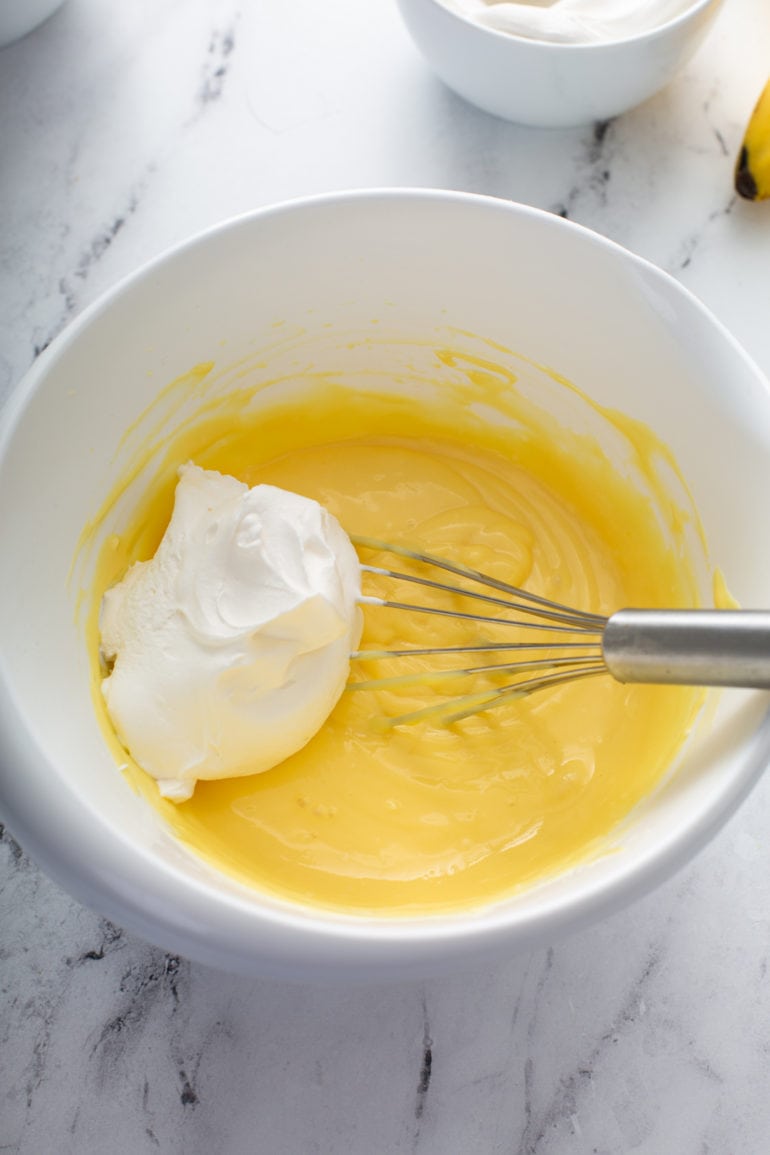 Whipped cream on top of the pudding mixture, the cream is being whisked into the mixture.