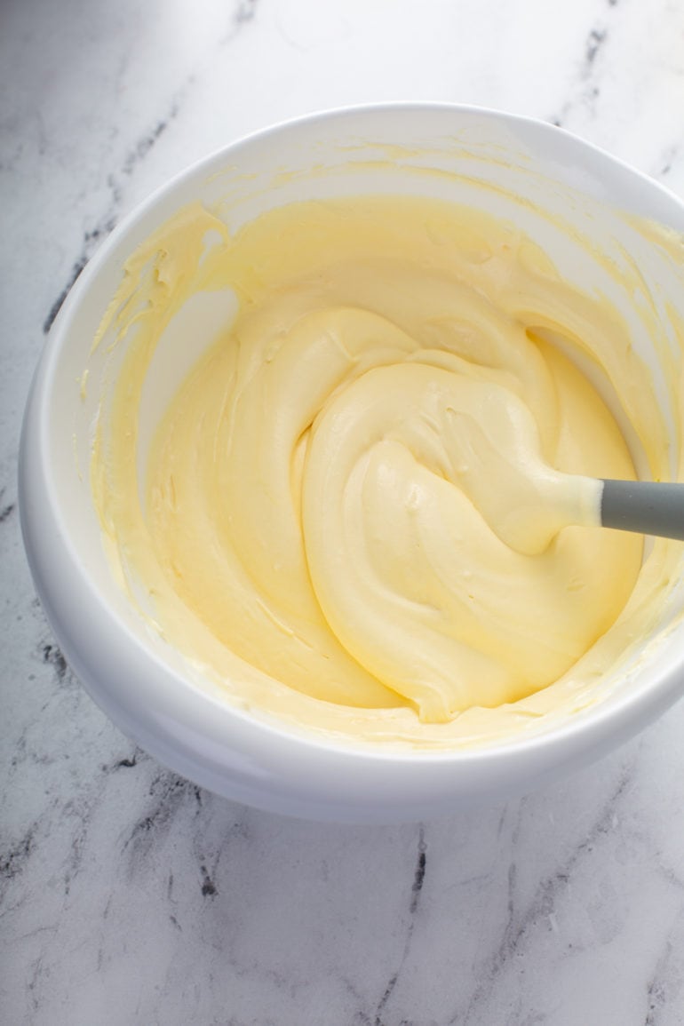 The fluffy, creamy, light yellow filling for dulce de leche banana cream pie. It is in a mixing bowl and a spoon is in the bowl.