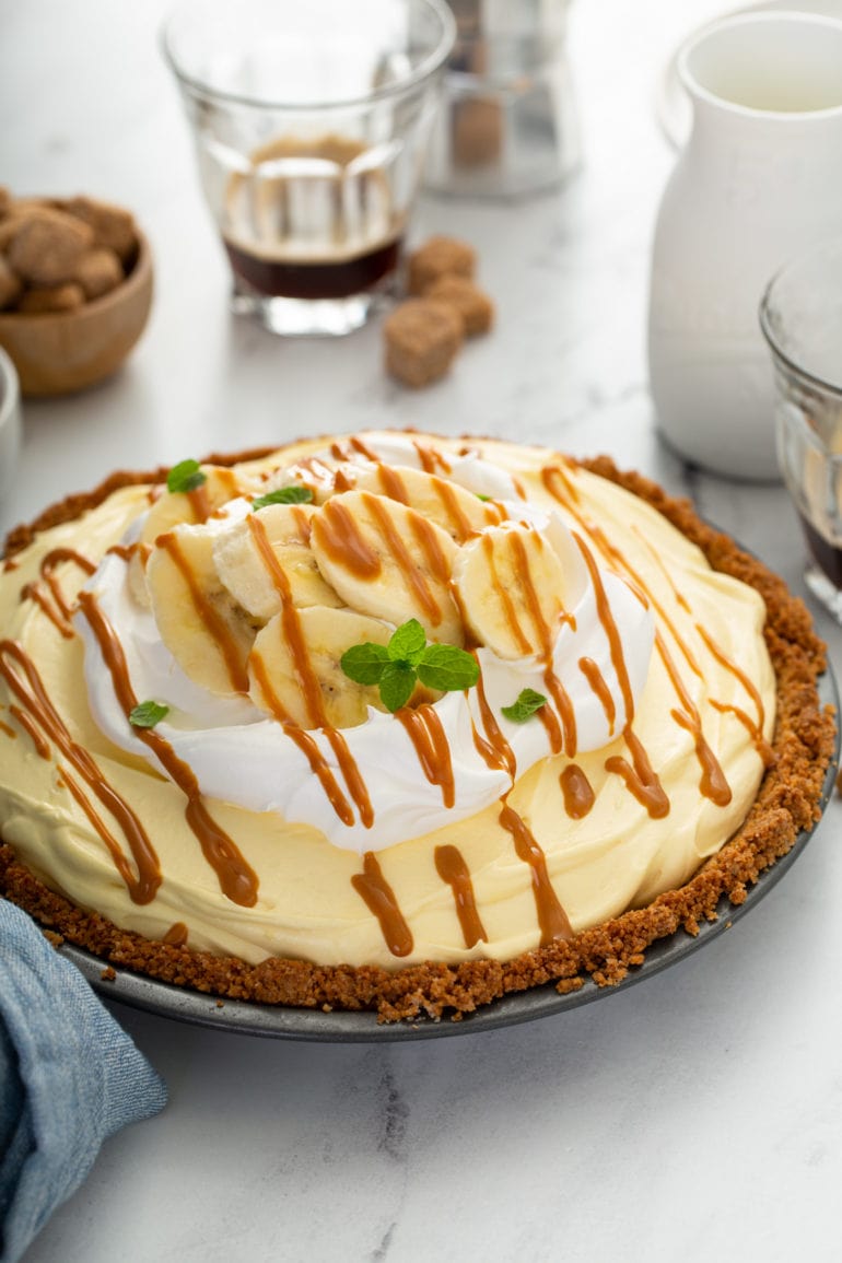 A banoffee pie in a graham cracker crust. the pie is topped with whipped cream and drizzled with dulce de leche.