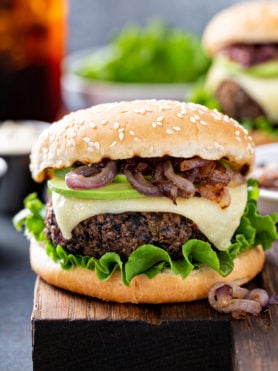 A black bean burger on a sesame seed bun. It is dressed with avocado, onions, cheese and lettuce.