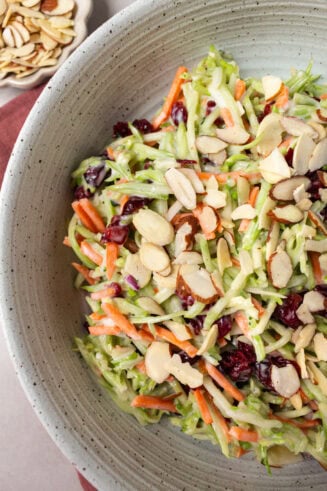 a photo of a large bowl full of broccoli slaw mixed with sliced almonds, craisins and carrot sticks
