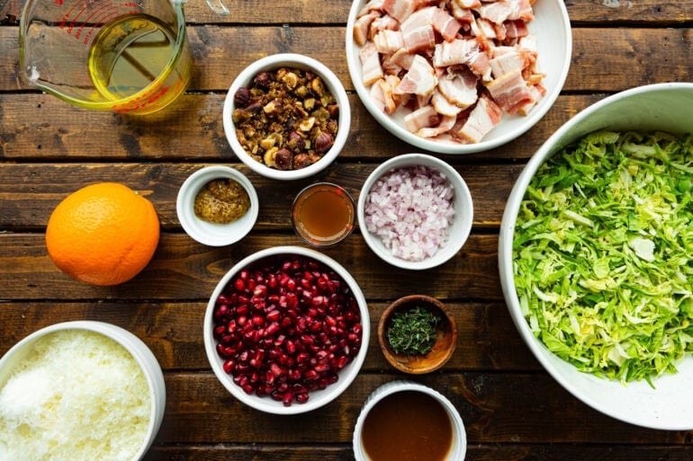 An overhead shot of the salad ingredients arranged on a counter, including fresh winter greens, bacon, pomegranate, Manchego cheese, hazelnuts, olive oil, apple butter, mustard, and fresh thyme.