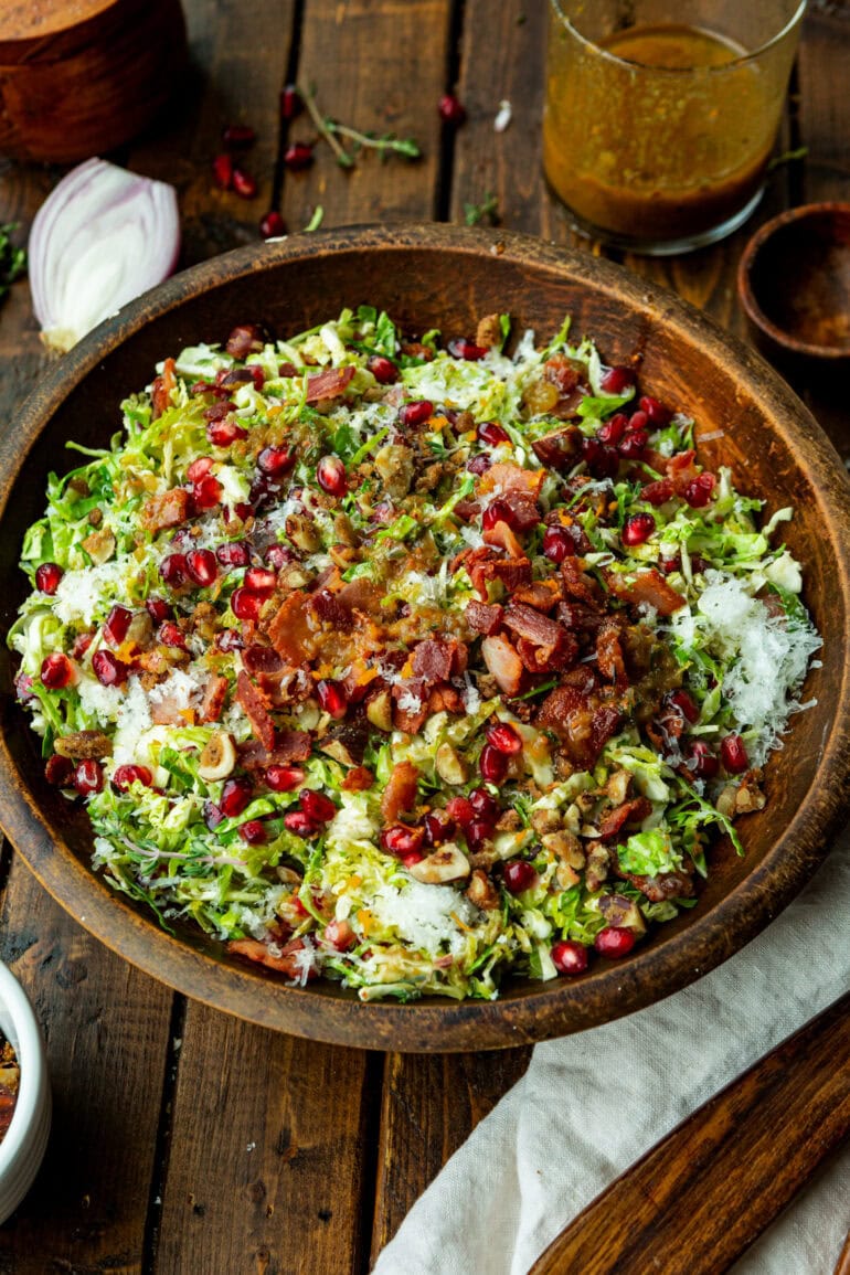 A bowl of pomegranate brussels sprout salad. The salad has brussels sprouts, bacon bits, pomegranate, and candied nuts.