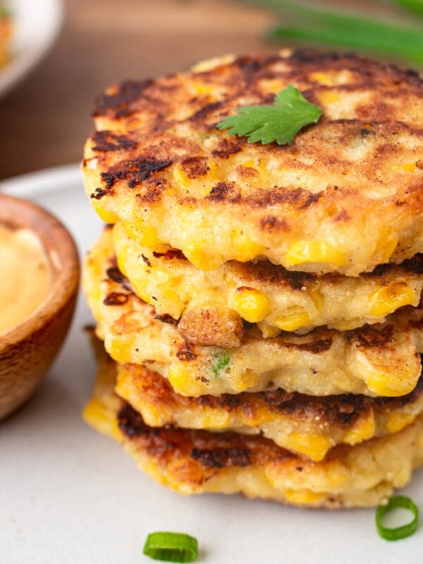 a photo of a stack of crispy golden cheesy corn fritters with a small bowl of dip next to it