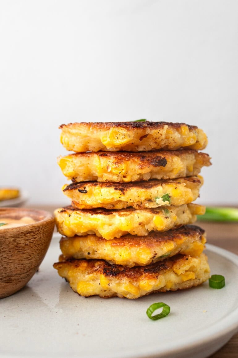 a photo of a stack of cheesy corn fritters with a small bowl of dip sitting next to it.