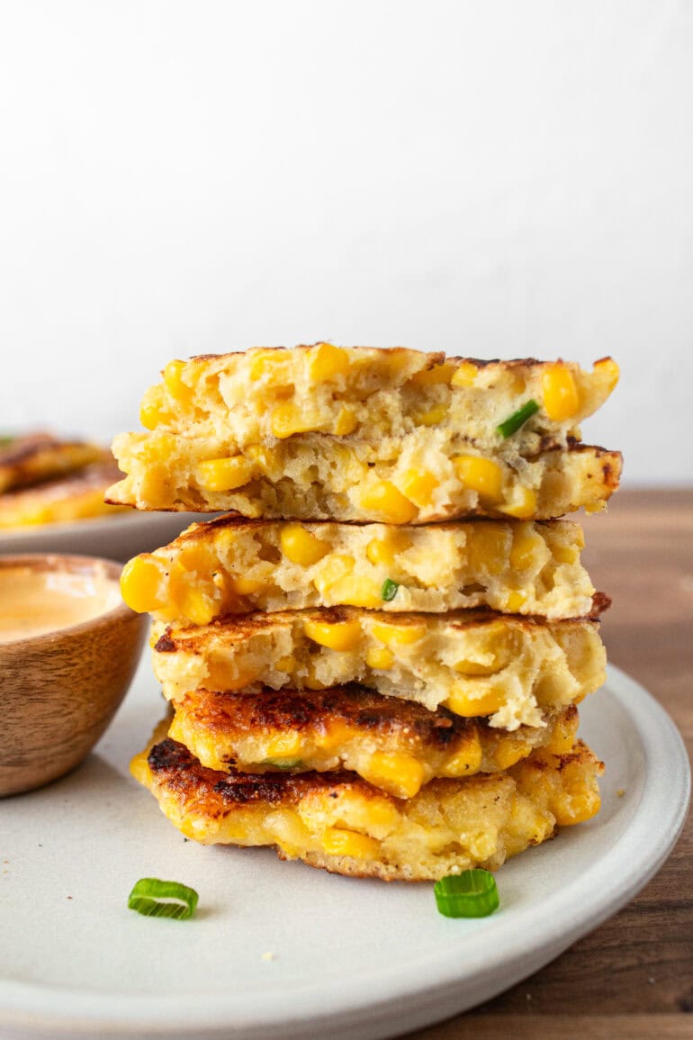 a photo of a stack of golden crispy corn fritters with a small bowl of dip on the side