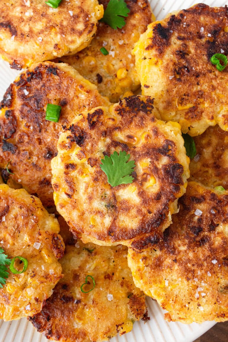 a photo of a pile of golden crispy corn fritters topped with chopped cilantro pieces