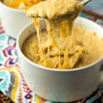 a white bowl full of cheesy grits and a spoon lifting it out of the bowl