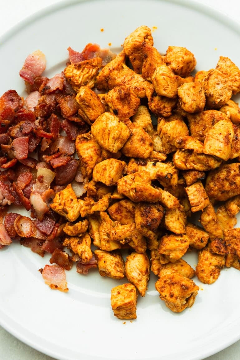 chunks of chicken breast being cooked with bits of crispy bacon