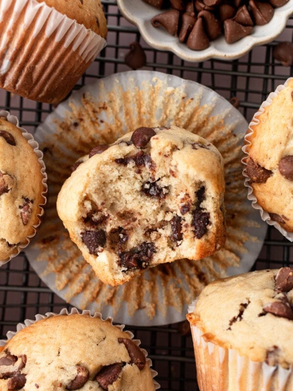 a photo of a chocolate chip cookie muffin laying on it's side with a bite taken out of it surrounded by whole muffins