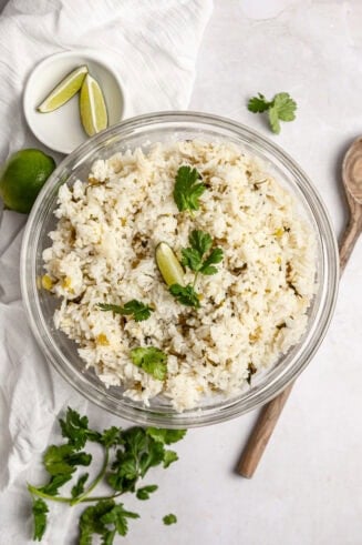 a photo of a large glass serving bowl full of fluffy rice with chopped cilantro on tope and a lime wedge