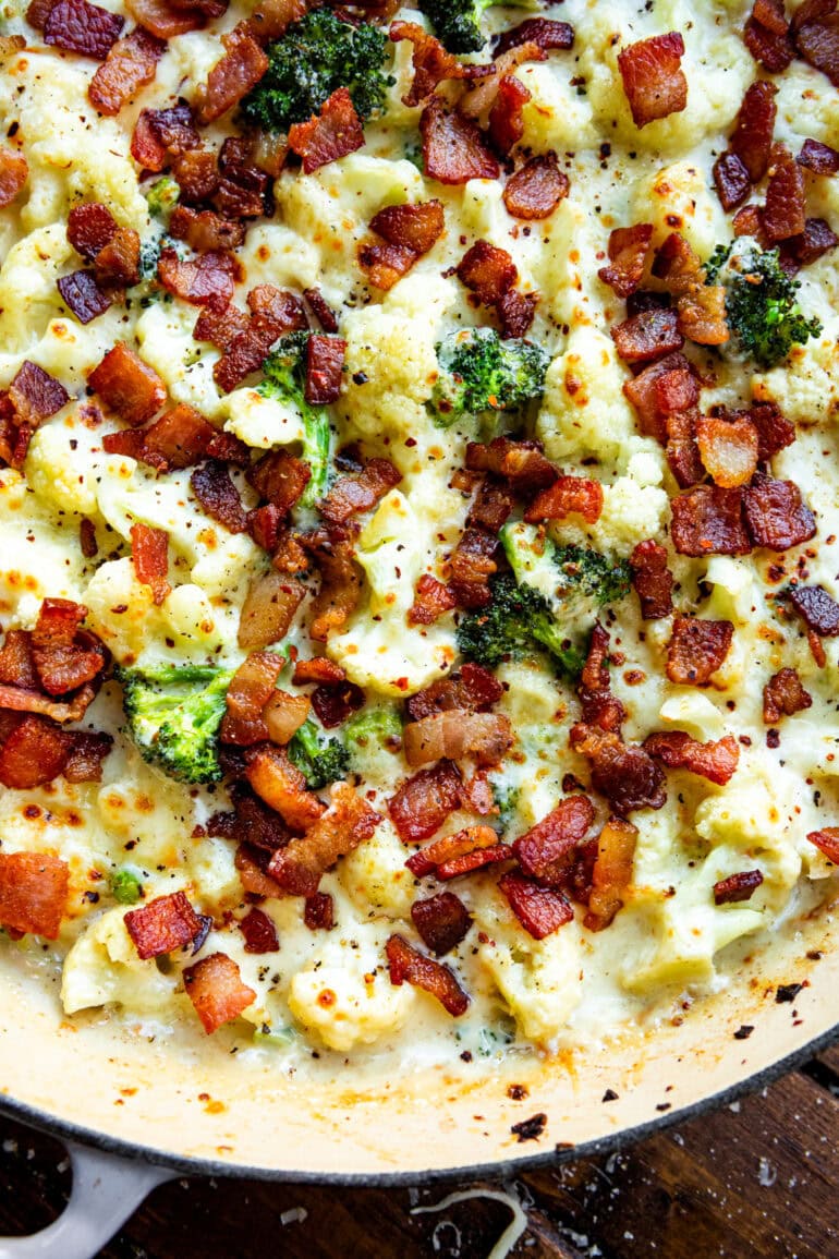 a photo of a baking dish full of creamy garlic parmesan broccoli and cauliflower topped with crispy bacon