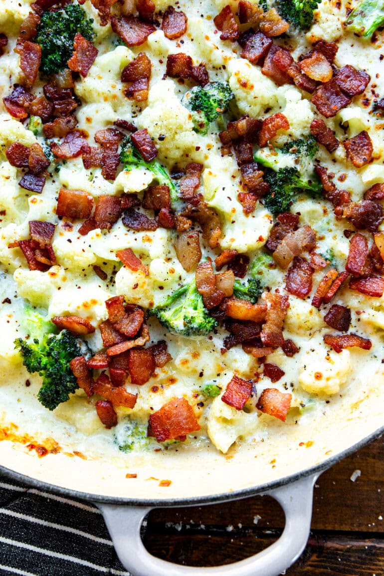 a photo of a skillet full of creamy garlic parmesan broccoli and cauliflower topped with crispy bacon