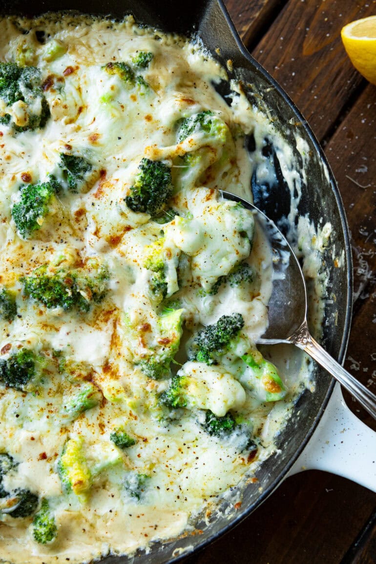 A picture of a frying pan filled with creamy garlic broccoli scalled with large metal spoon