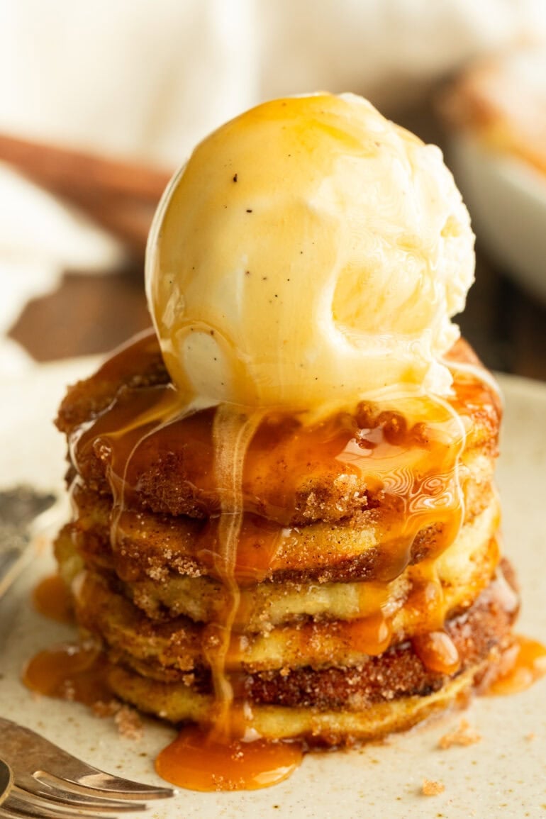 a stack of golden fried apple rings topped with a scoop of vanilla ice cream and drizzled with warm caramel