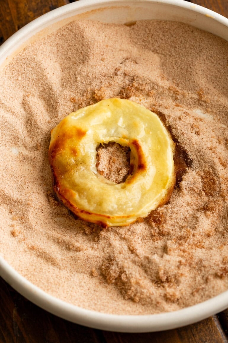 a golden battered fried apple ring sitting in a bowl of cinnamon sugar
