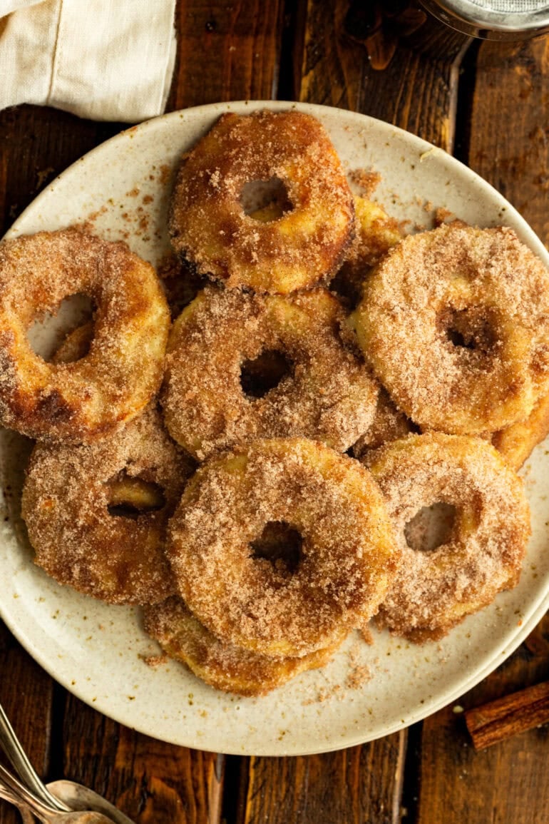 several golden fried apple rings coated in cinnamon sugar sitting on large serving plate