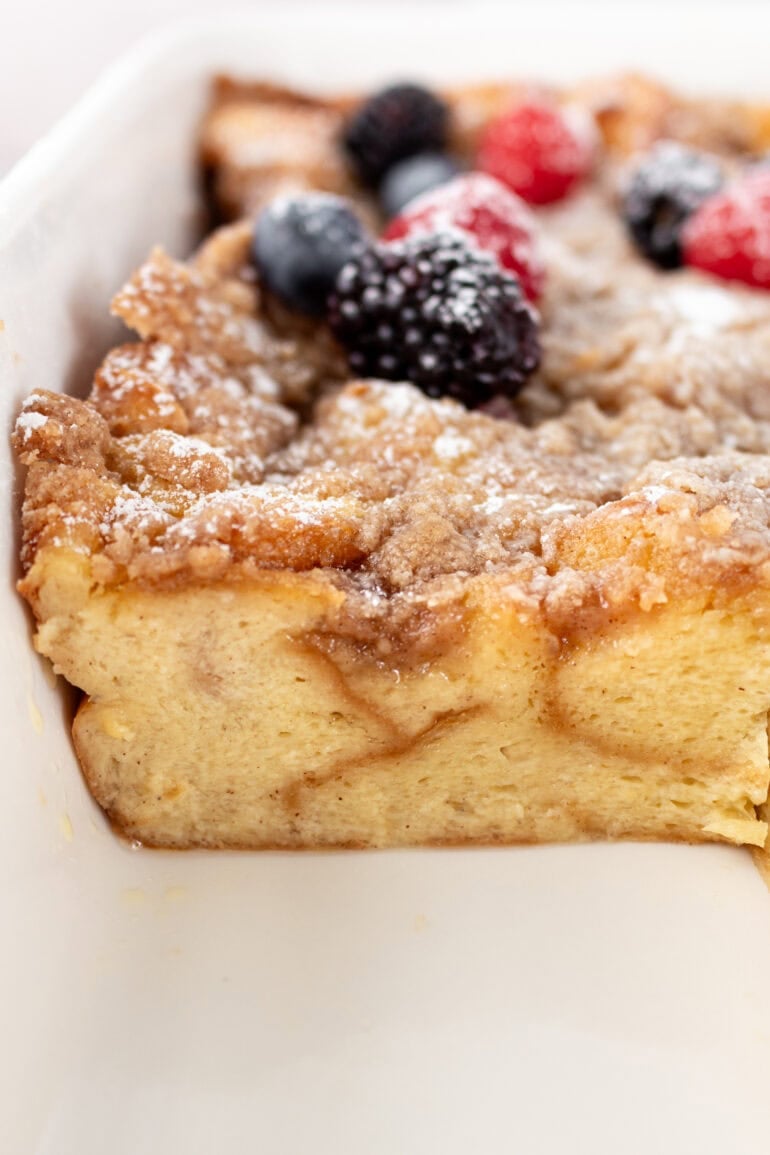 A photo of a slice of French toast casserole removed from the entire pan and topped with powdered sugar and fresh berries