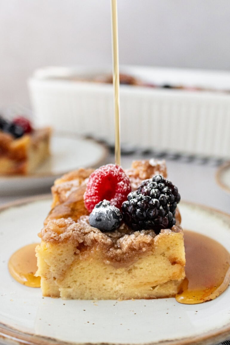 Photo of someone pouring syrup over a French toast casserole with fresh berries on top