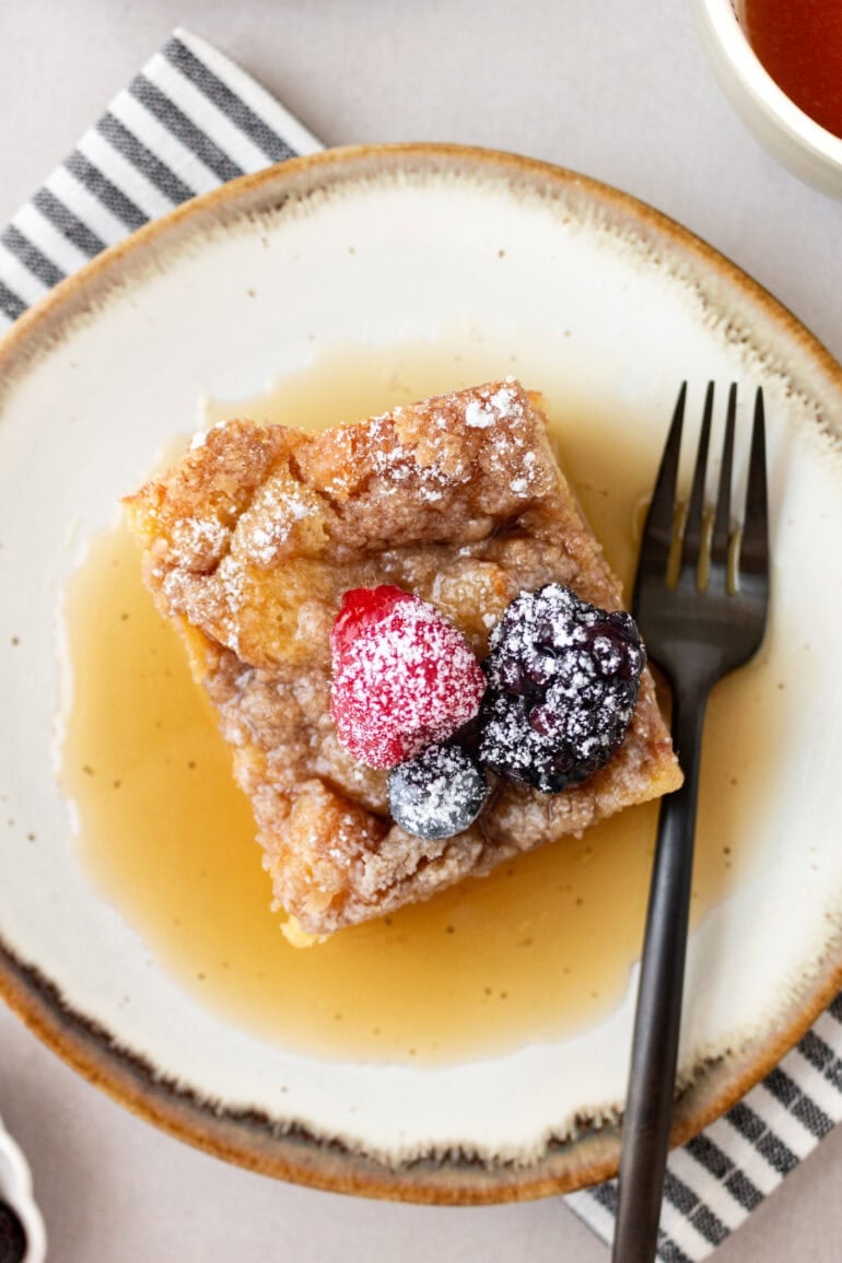 A photo taken on top of a French toast casserole with fresh berries and powdered sugar sitting on top of gin and a pool of syrup