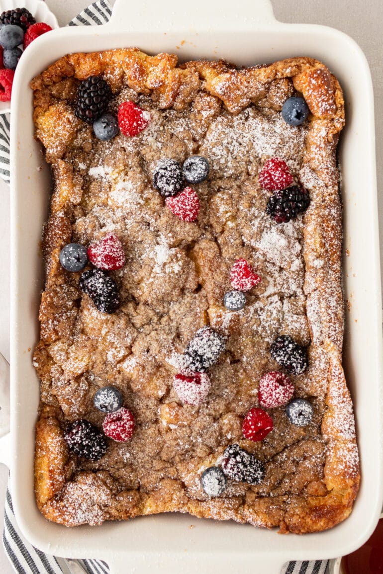 A photo of a fully baked French toast casserole with streusel and topped with fresh berries and powdered sugar