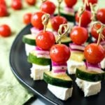 Greek Salad Skewers - Cherry tomatoes, cucumber, and red onion are tossed in a homemade Greek vinaigrette and layered on mini skewers with a little square of feta cheese.