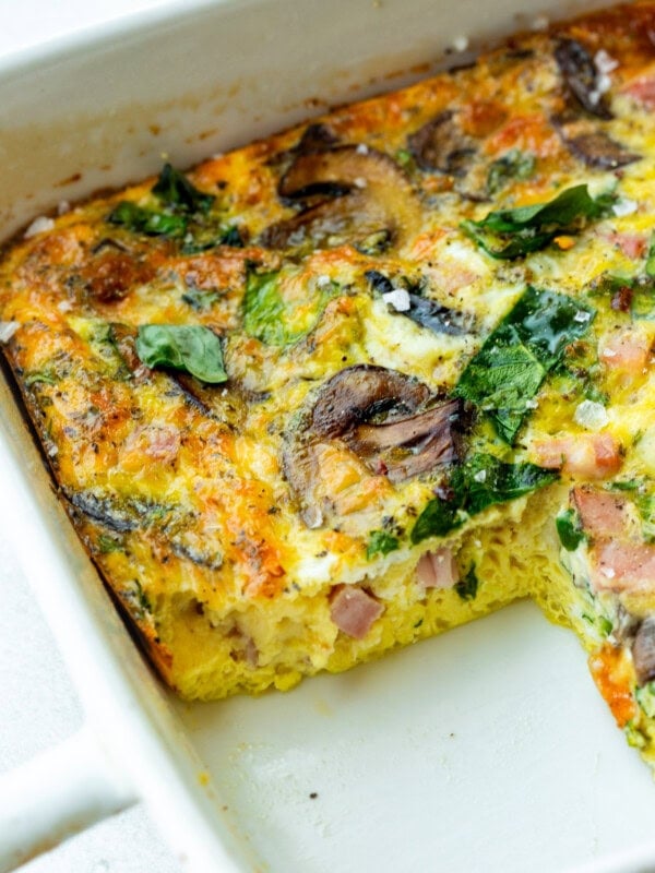 a baking dish of a baked egg, spinach and sauteed mushroom casserole with a serving missing so you can see the cross-section of the casserole