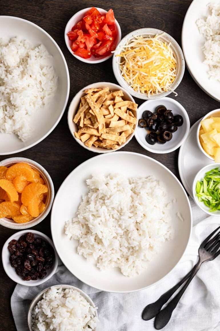 All the fresh Hawaiian Haystacks ingredients laid out before assembly, including fluffy white rice, pineapple, celery, tomatoes, cheddar cheese, green onions, and crispy wonton strips.