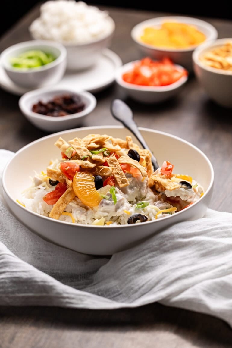 Coconut milk chicken sauce draped over rice in a white bowl, finished with colorful toppings.