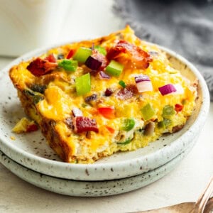 a serving of baked egg casserole with bacon and peppers sitting on a small plate