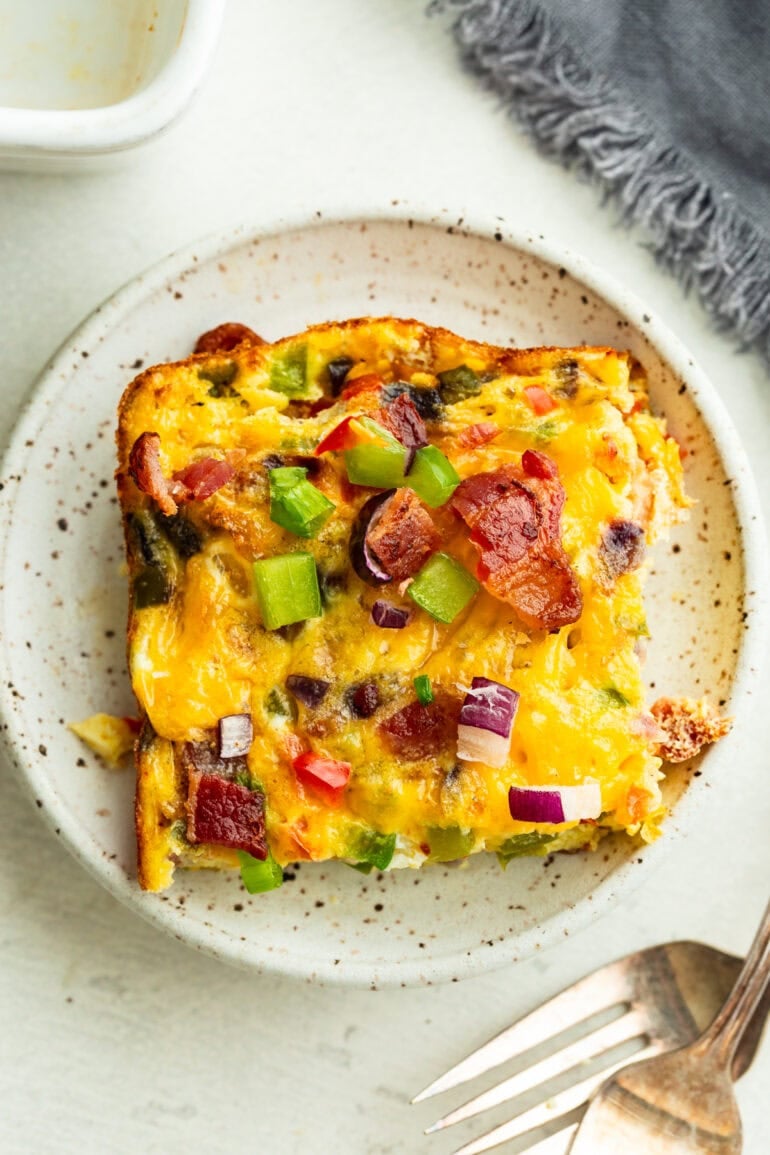 A square cheesy baked egg casserole with bacon and peppers, sprinkled with chopped red onions