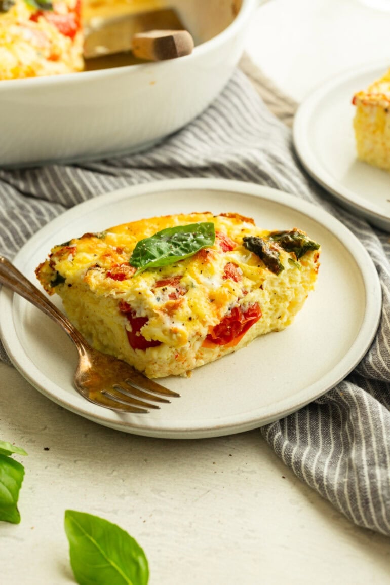 a serving of breakfast egg casserole loaded with cherry tomatoes, roasted red peppers and fresh basil