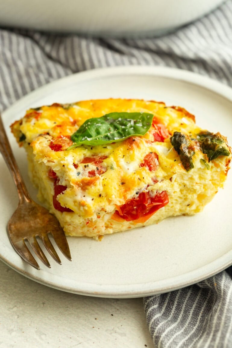 a serving of fluffy egg casserole with basil and tomatoes on a white plate