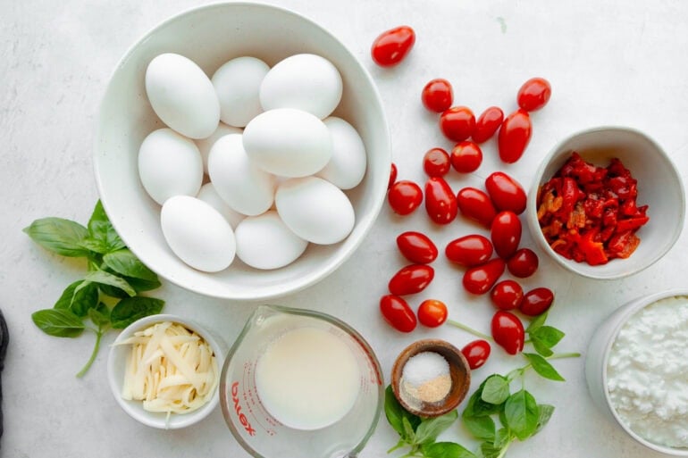 all the ingredients for a cottage cheese egg bake including cherry tomatoes, eggs, fresh basil, salt, milk, mozzarella cheese